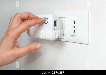 Donna accendere un ripetitore wifi collegato a una presa a muro Foto Stock
