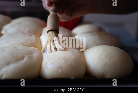 Verniciatura del latte su panini crudi. ,facendo i rulli di pane a hobby di casa., Foto Stock