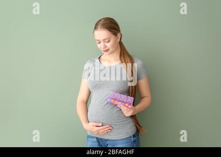 Giovane donna incinta con scatola di pillole su sfondo colore Foto Stock