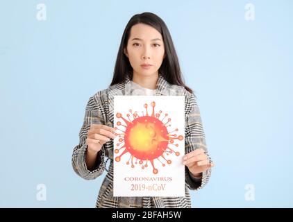 Donna asiatica che tiene foglio di carta con foto di Coronavirus su sfondo a colori Foto Stock