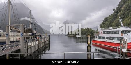 MILFORD SOUND, NUOVA ZELANDA - Novembre 21 2019: Paesaggio con navi passeggeri turistiche al molo sotto nuvole basse in località turistica, girato in brigg Foto Stock