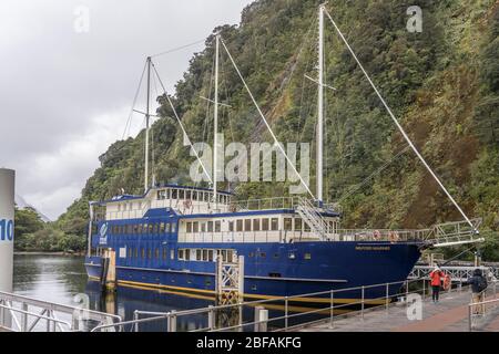 MILFORD SOUND, NUOVA ZELANDA - Novembre 21 2019: Paesaggio con nave turistica passeggeri al molo sotto nuvole basse in località turistica, girato in brigh Foto Stock