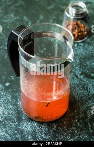 Acqua o tè Sumac e spezie Sumac rosso macinato essiccato con chiodi di garofano in French press. Pronto a bere. Foto Stock