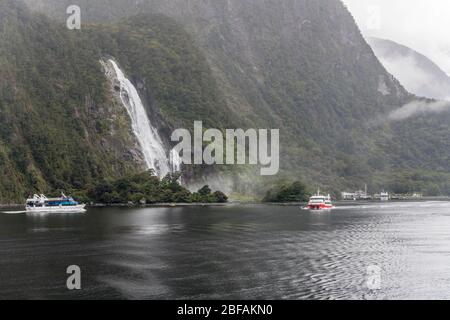 MILFORD SOUND, NUOVA ZELANDA - Novembre 21 2019: Paesaggio con navi passeggeri e flotilla kayak in fiordo a Bowen Falls, girato in luce brillante su no Foto Stock