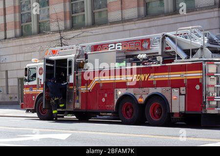 un vigile del fuoco accanto a un camion per motori antincendio. Legge la scala 26 Harlem, parte del Dipartimento dei Vigili del fuoco di New York o FDNY Foto Stock