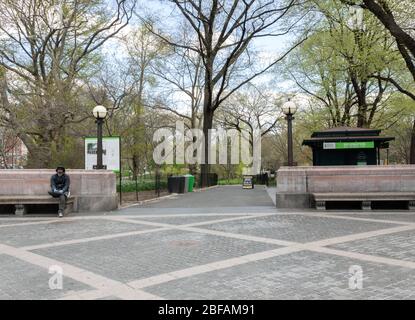 Un uomo in maschera facciale siede da solo all'ingresso del Columbus Circle in un Parco Centrale vuoto durante il coronavirus o la pandemia del covid-19 Foto Stock