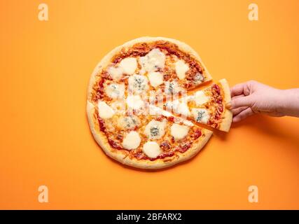 Quattro formaggi pizza e una donna mano prendendo una fetta di pizza, su uno sfondo arancione senza cuciture. Piatto con pizza al formaggio 4. Deliziosa cucina italiana Foto Stock