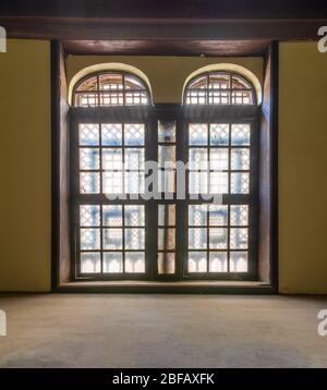 Grande finestra vintage con ornamento situata all'interno di una stanza vuota con pareti gialle e pavimento in legno Foto Stock