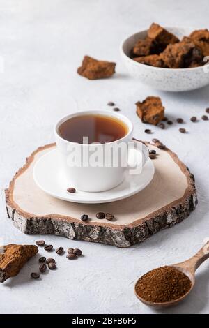 Funghi chaga e caffè su sfondo chiaro. Bevanda salutare alla moda. Formato verticale. Primo piano. Foto Stock