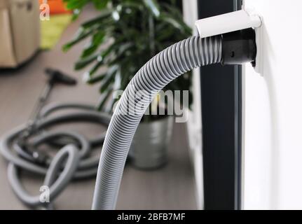 Raccordo del tubo flessibile dell'aspirapolvere centrale collegato alla presa di ingresso a parete. Vista nella stanza con aspirapolvere centrale. Foto Stock