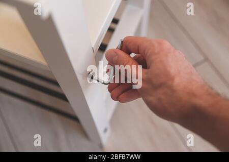 Montaggio di mobili, chiave esagonale di chiusura a mano, vite per mobili avvitata nella tavola di banco. Foto Stock