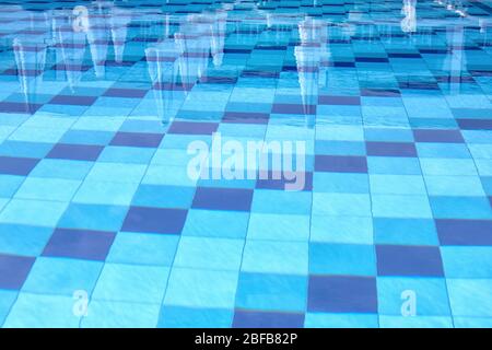 Piscina con fondo blu. Vacanze in estate. Superficie dell'acqua con riflessione di ombrelli e piastrelle sul fondo. Blu trasparente wa Foto Stock