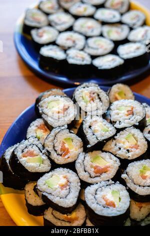 Due piatti rotondi di sushi maki fatti in casa con salmone, riso e avocado su tavola di legno