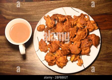 Chai con pakora e bhajiya e servito su piatto su sfondo di legno Foto Stock