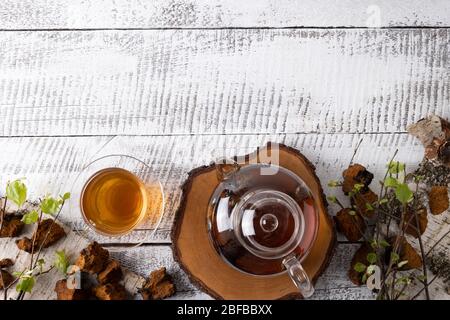 Infusione di funghi chaga in teiera di vetro su tavola bianca. Vista dall'alto. Spazio di copia. Foto Stock