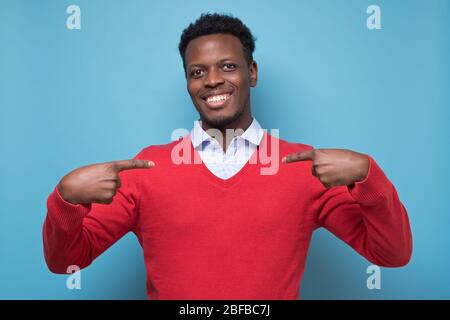 Giovane africano in pullover rosso che si sente orgoglioso e di sé trionfo assicurato Foto Stock