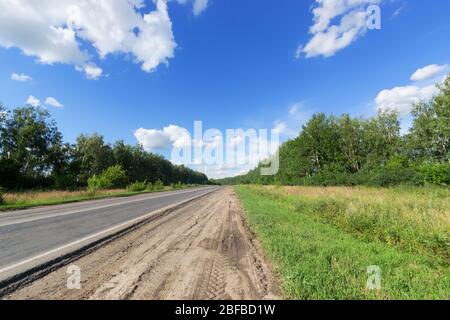 Strada asfaltata e non asfaltata, tra gli uccelli sotto il cielo blu Foto Stock