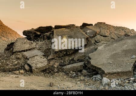 Macerie su un cantiere stradale, asfalto rotto e pezzi di bitume strato di un manto stradale dalla demolizione di una strada al tramonto Foto Stock