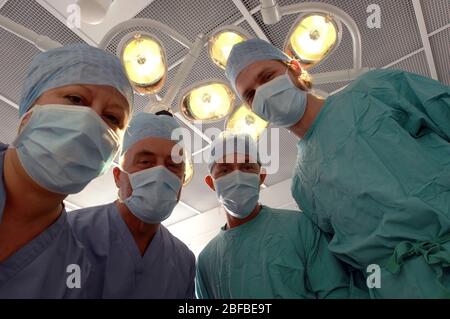 Una vista del paziente di un team di chirurghi mascherati sotto le luci in un teatro operativo ospedaliero. Foto Stock