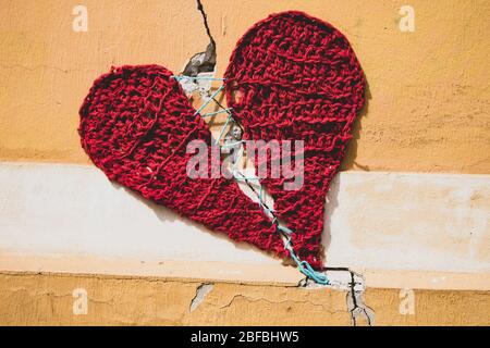 Maglia cuore rosso cucito intorno frattura parete su facciata beige, filmato in vie Zagabria Foto Stock