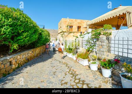 I turisti e gli asini che trasportano i turisti a piedi uno stretto sentiero in pietra vicino a Lindos sull' isola di Rodi, Grecia. Foto Stock