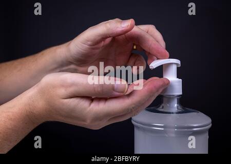 Mano che riceve e mano che aziona il rubinetto di un gel disinfettante a base di alcool su uno sfondo scuro. Studio di istruzioni sulla disinfezione Foto Stock