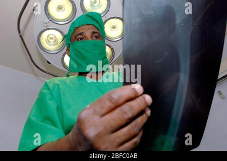 Un radiologo esamina una radiografia sotto le luci chirurgiche per sala operatoria Foto Stock