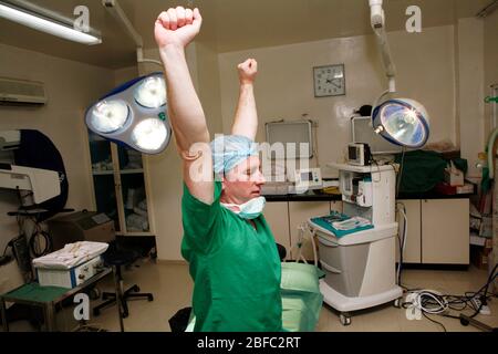 Un chirurgo stanco sopravlavorato allunga le braccia mentre si siede su un tavolo operatorio Foto Stock