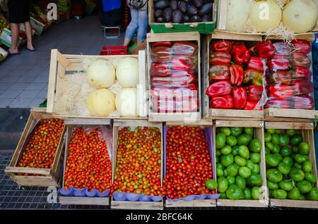 Venditore di mercato di strada con generi alimentari. Verdure e frutta in scatole di legno fuori sulla strada vicino al negozio. Peperone rosso, pomodori ciliegini, melone e sm Foto Stock