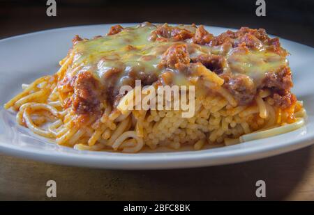 spaghetti bolognese con formaggio fuso sulla parte superiore, in un piatto bianco su fondo nero Foto Stock