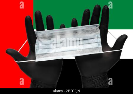 Medico che tiene maschera medica per il viso in due mani guanti neri sullo sfondo bandiera nazionale degli Emirati Arabi Uniti. Quarantena concettuale, pandemia Foto Stock