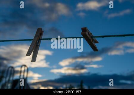 due spille di vestiti agganciati ad una linea vuota dei vestiti con le goccioline d'acqua da dopo una pioggia in un cortile urbano o rurale che simboleggia il lavoro domestico o il lavaggio Foto Stock