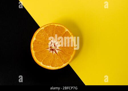 Fette di agrumi freschi di frutta arancione su sfondo nero e giallo. Fotografia creativa in studio Foto Stock