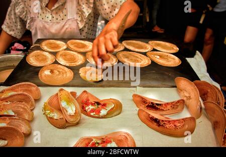 Vendita di cibo di strada che cucina e vende spuntini tradizionali chiamati khanom bueang o crepe croccante thailandese, mostrando la cultura locale e la cucina della Thailandia Foto Stock