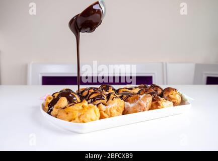 Cioccolato Profiterolo. Dessert dolce su piatto bianco. Profiteroles fatti in casa con crema e salsa al cioccolato. Foto Stock