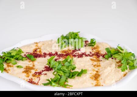 Humus fatto in casa su un piatto bianco con tahini, piccante, olio d'oliva, limone, prezzemolo e ceci. Cibo arabo, antipasto - humus delizioso. Messa a fuoco selettiva Foto Stock