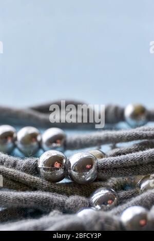 Natale, inverno o gioielli sfondo. Fili a maglia grigia fatti a mano con perle d'argento intemperate e graffiate su sfondo blu. Foto Stock