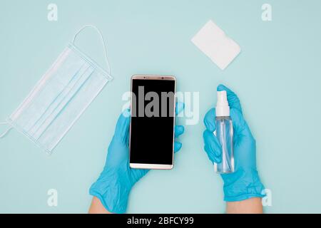 Mani che indossano guanti protettivi per la pulizia e la disinfezione del telefono cellulare Foto Stock