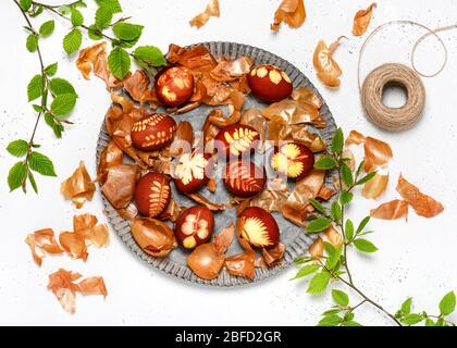 Uova di Pasqua tinte con bucce di cipolla e modello di foglie fresche di piante in una piastra metallica rustica. Concetto fai da te. Vista dall'alto. Foto Stock