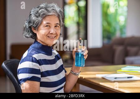 Ritratto di donna anziana asiatica che mostra igienizzante mano pompando gel di alcol e lavando prima di lavorare in casa da periodo, coronavirus o covid Foto Stock