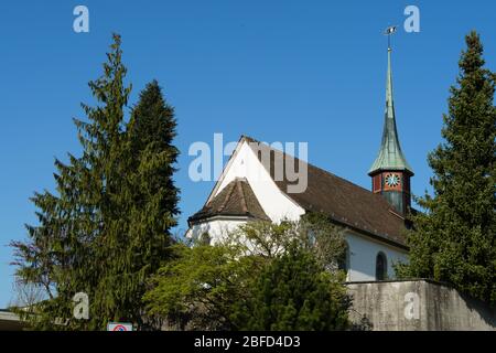 Vecchia chiesa riformata a Urdorf, Svizzera circondata da alberi, vista laterale con particolare della torre della chiesa in un giorno limpido in primavera. Foto Stock