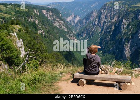 Donna sulla panca in legno sulla pittoresca estate Tara canyon in montagna Parco Nazionale del Durmitor, Montenegro, Europa Balcani Alpi Dinariche, UNESCO World H Foto Stock