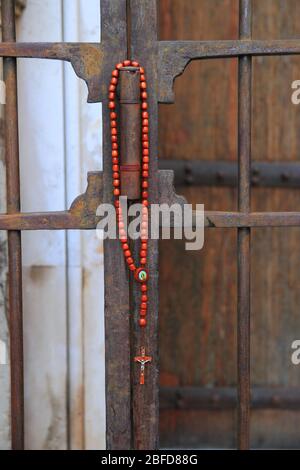 Corona di un rosario con crocifisso posto da un fedele sulla porta chiusa del Santuario di nostra Signora dei Polli, durante il periodo di chiusura Foto Stock