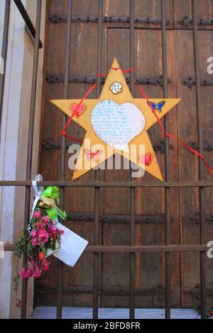 Una carta a forma di stella colorata con una poesia dedicata alla Madonna del Carmelo e fiori legati al cancello chiuso, durante l'emergenza dal covid-19. Foto Stock