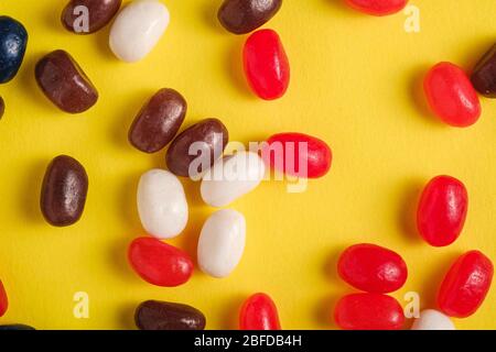 Succosa frutta dolce fagioli di gelatina colorati su sfondo giallo brillante, vista dall'alto macro Foto Stock