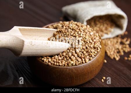 Semole di grano saraceno (semi di colmi) in ciotola di legno con cucchiaio, primo piano. Grano saraceno intero su sfondo legno, fuoco selettivo Foto Stock