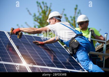 Due tecnici addetti che collegano pannelli fotovoltaici solari pesanti a piattaforme in acciaio. Installazione esterna di sistemi solari, concetto alternativo di generazione di energia verde rinnovabile. Foto Stock