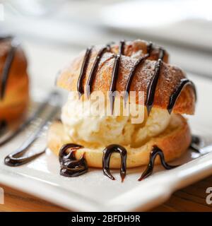 Profiterolo, una palla di pasta choux francese ripiena con un tipico dolce e umido ripieno di gelato alla vaniglia, caramello salato, salsa al cioccolato Foto Stock