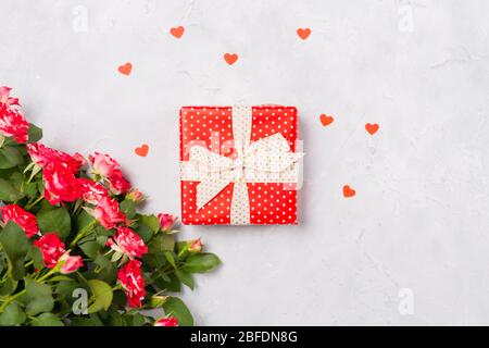 Confezione regalo rossa e rose rosse su sfondo bianco con confetti a cuore rosso. Regalo di Natale, sorpresa di San Valentino, idea di compleanno di festa della mamma. Piatto Foto Stock