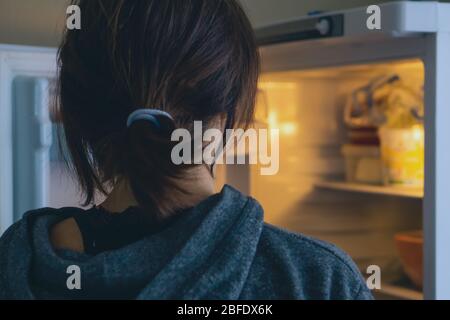 Vista posteriore di una donna che guarda in frigorifero aperto a casa o cucina. Foto Stock